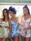 Three women in satin sleepwear sets standing in a room with a window in the background.