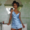 Woman in a cloud blue satin sleepwear set standing in a bathroom with green tiles.
